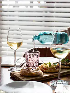 Glass of white wine, water bottle, and food on table.