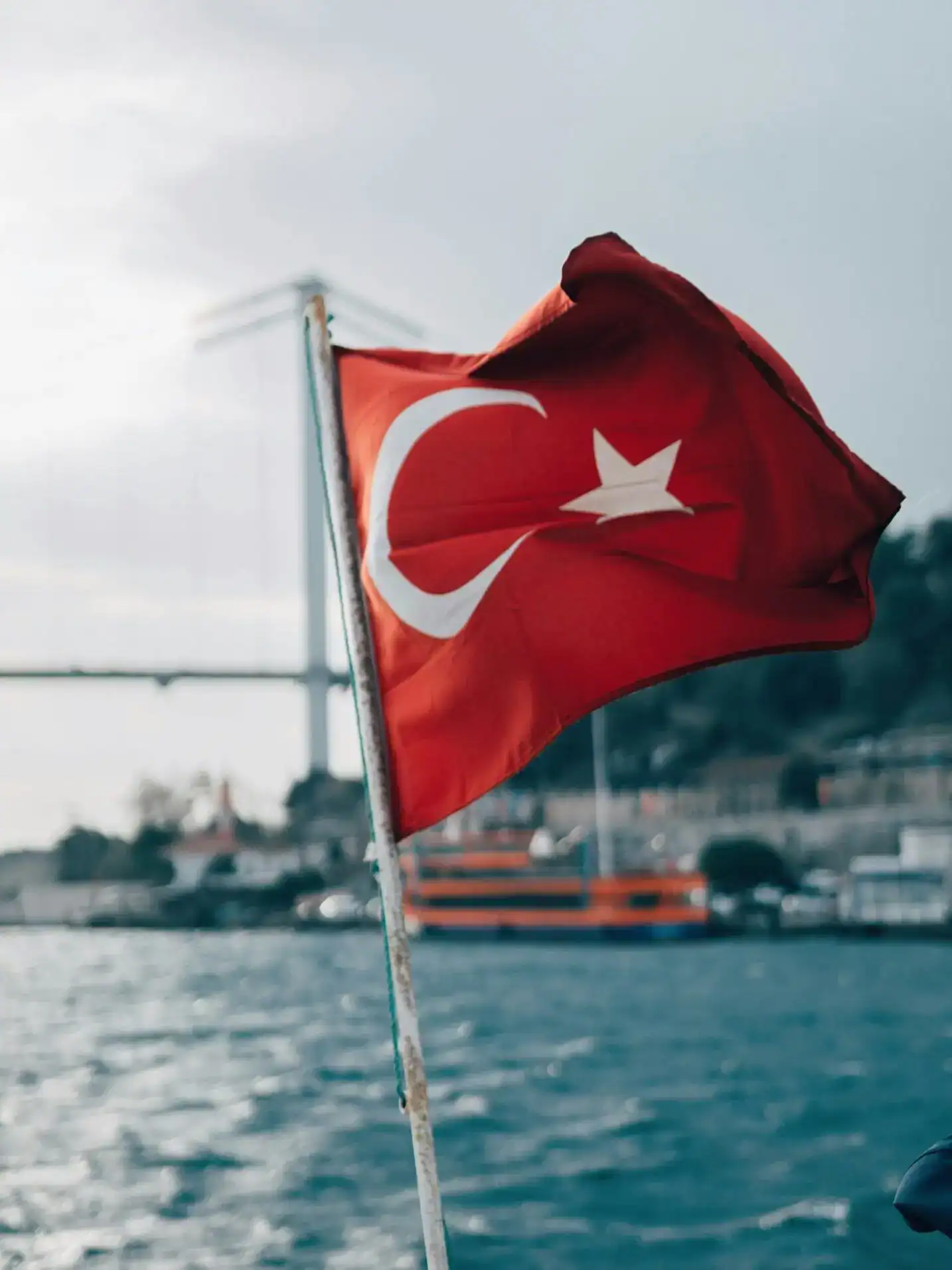 Turkish flag waving on the water with boats in the background.